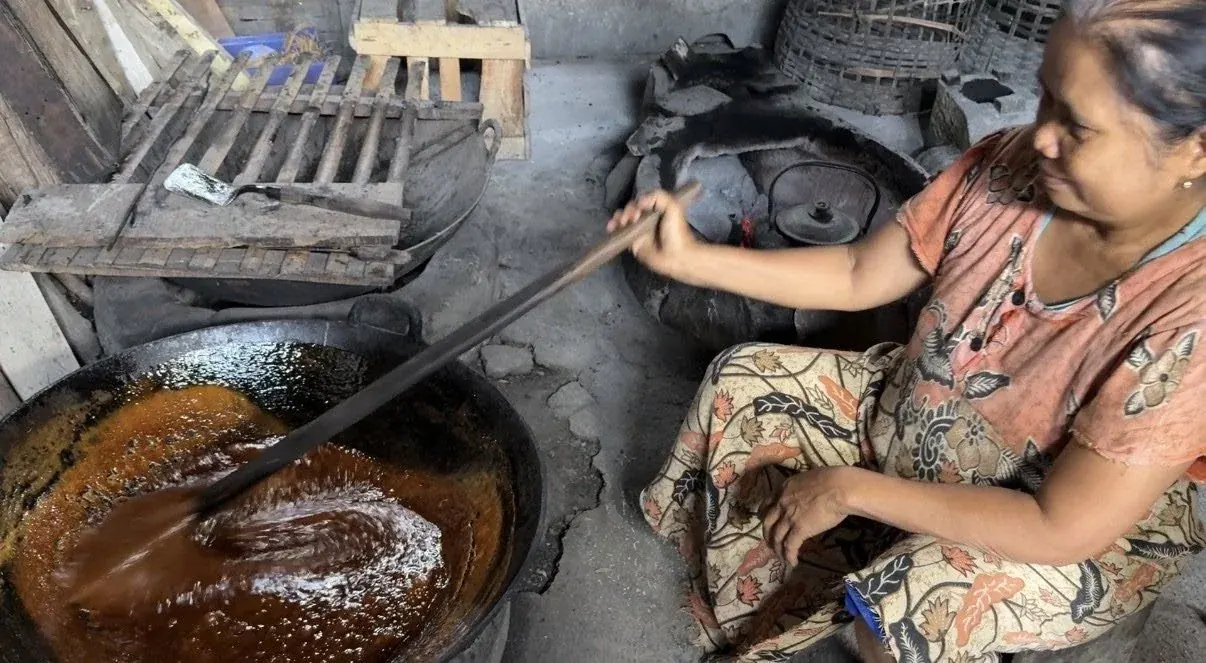 Perempuan memasak nira kelapa di tungku dapur rumah